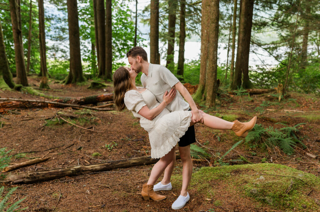 Guy holds girl leg up and dipping down for a romantic kiss in the forest.