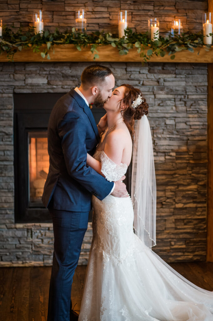 Bride and groom kiss at the alter with fireplace and candles in the back of them.