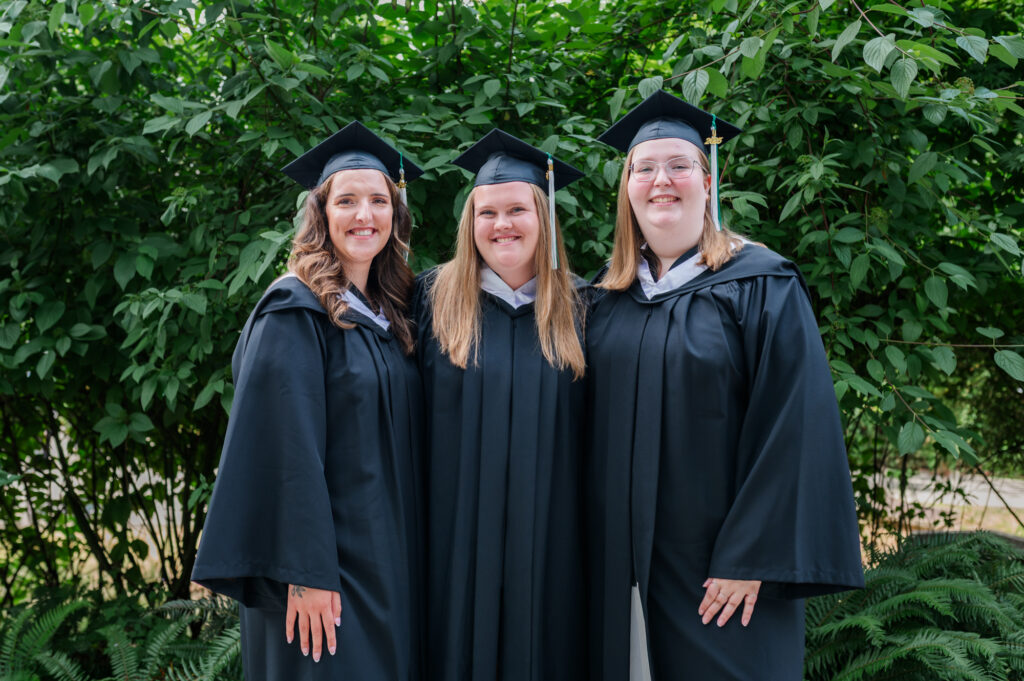 Grad students lean in close for a photo at UFV campus and greenery in the back round. 