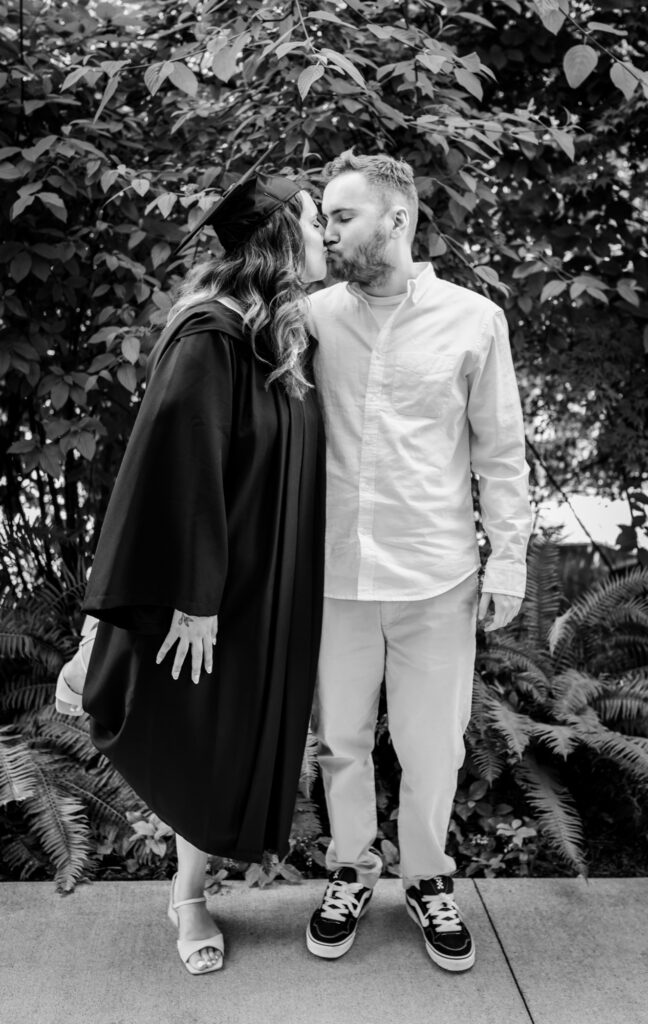Black and white grad photo of Jessica kissing her boyfriend on the day of her graduation.