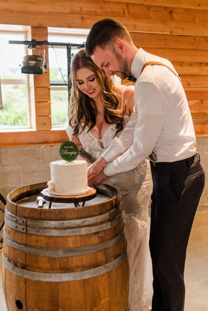 Bride and groom cutting into their cake for the first time, both couple smiling and looking down at the cake. 