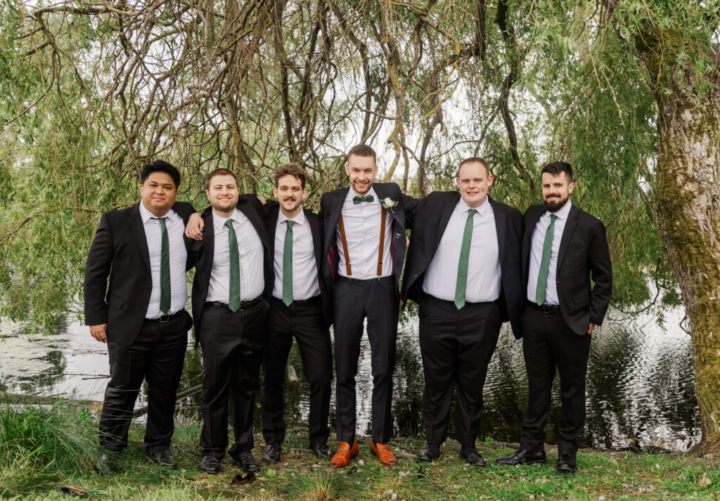 Groom and his best friends pose in front of a willow tree.