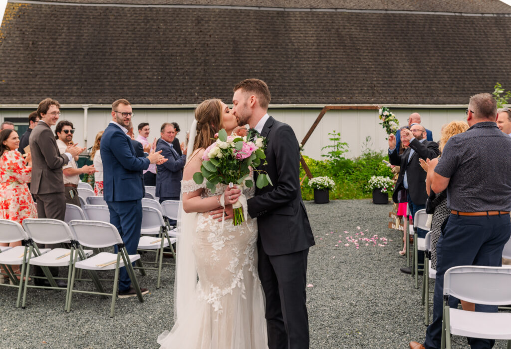Bride and groom kiss in the middle of the aisle and guests looking and clapping.