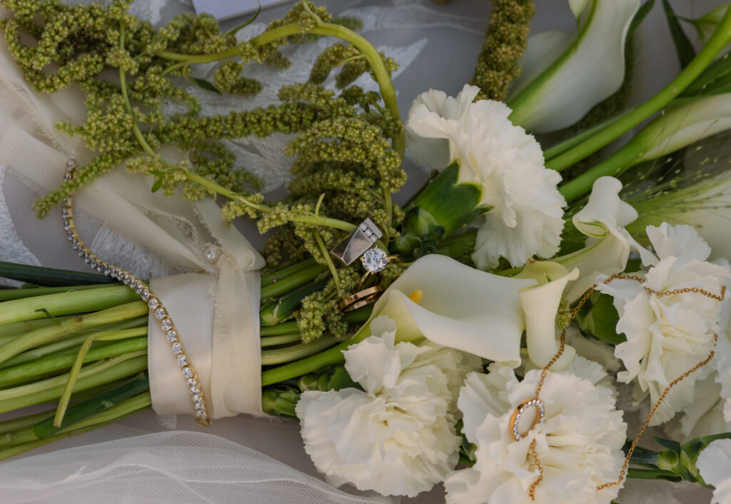 Close detail shoot of wedding rings and necklace on flower bouquet.