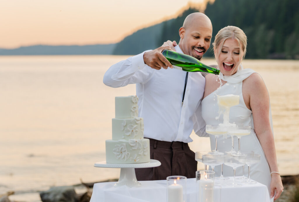 Groom pouring the champagne on the champagne tower to fill the glasses. Bride is smiling looking at champagne tower and is over joyed.