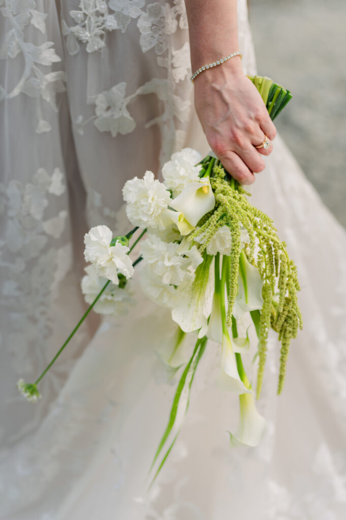Flower bouquet detail wedding day shoot with white floral brides dress in the back round.