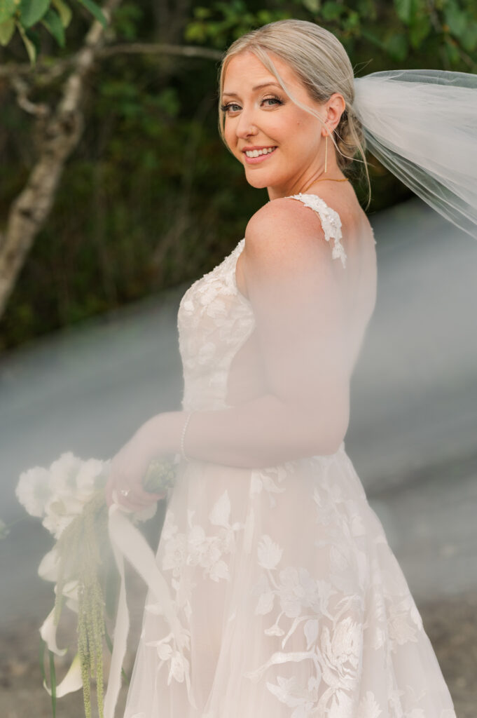 Bride looking at the camera and her veil across her body and she is holding her flower bouquet at her waist. 