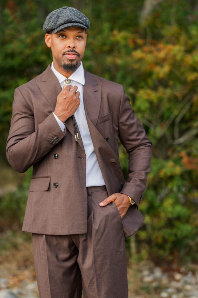 Groom in brown wedding suite holding his tie with his right hand and looking away in the distance. 