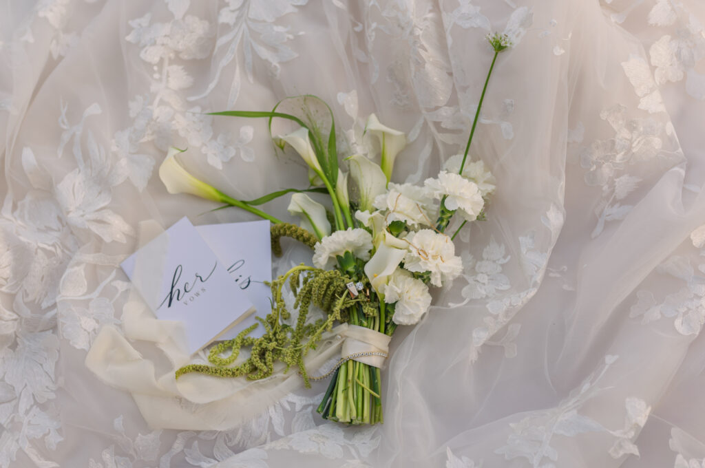 Wedding details of dress, floral bouquet, rings and wedding vow books.