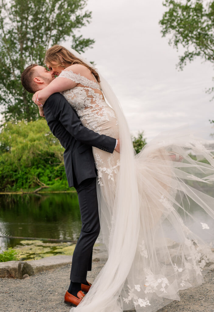 Groom lifts bride for a romantic kiss her arms holding his upper shoulders and brides legs lifted up.