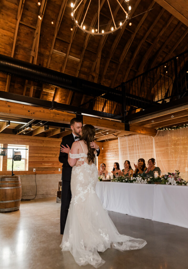 Bride and groom first dance at their reception. Bridesmaids smiling and clapping in the back round.