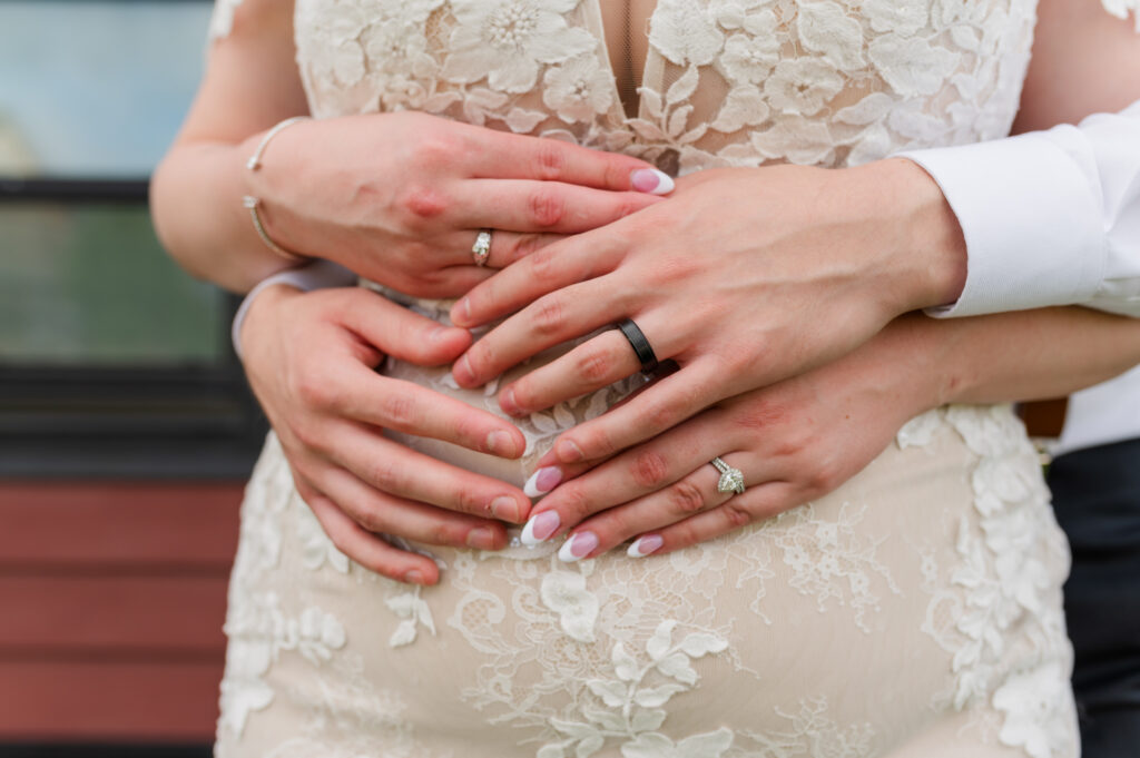 Bride and groom holding hands, photos has their wedding bands and touching finger tips.