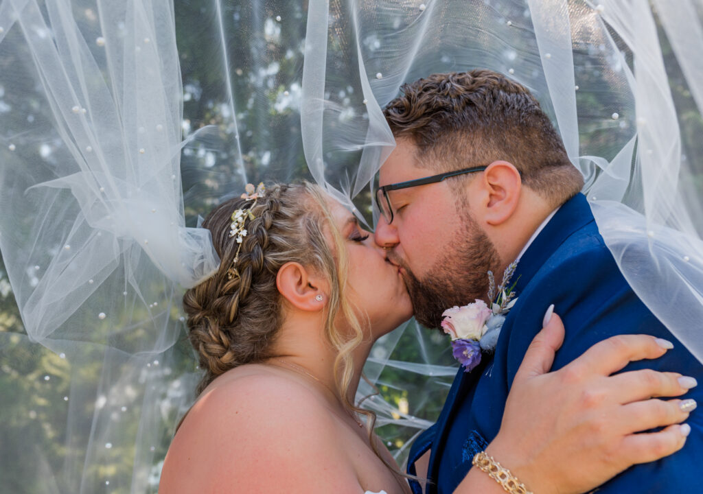 Bride and groom under the veil having their first kiss Langley BC. 