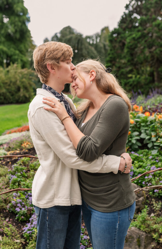 Just Engaged young guy kisses girlfriends forehead at Queen Elizabeth Park, Vancouver BC.